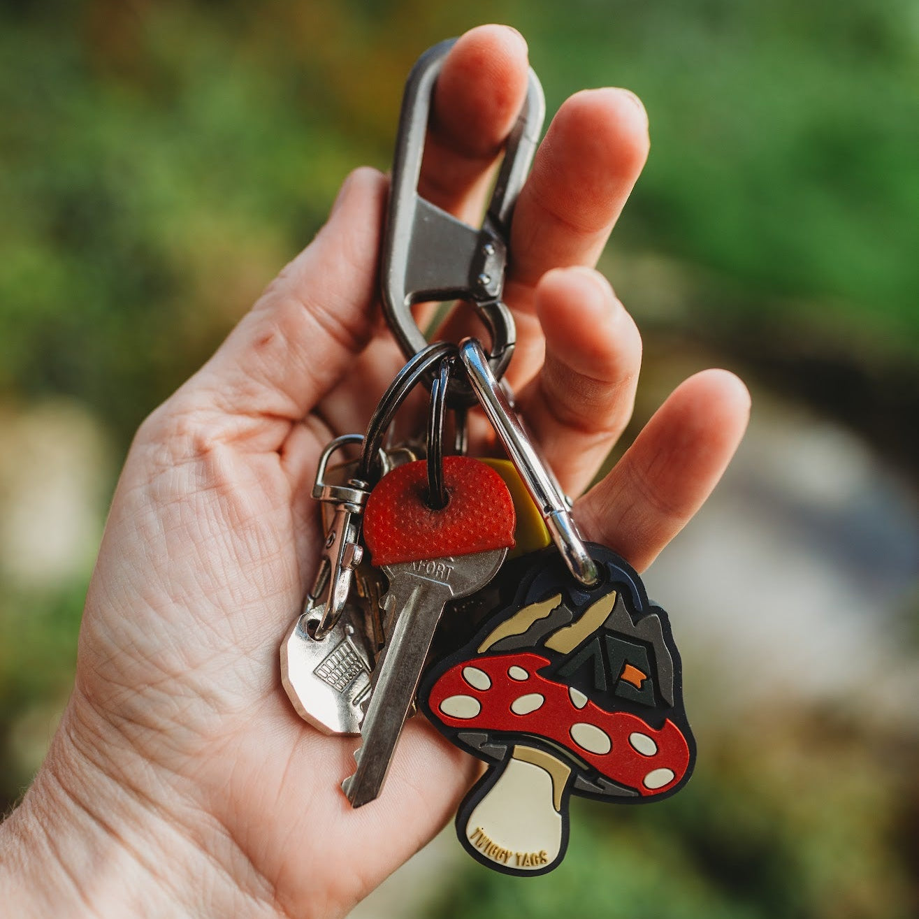 Hand holding a keychain with a mushroom design against a blurred natural background